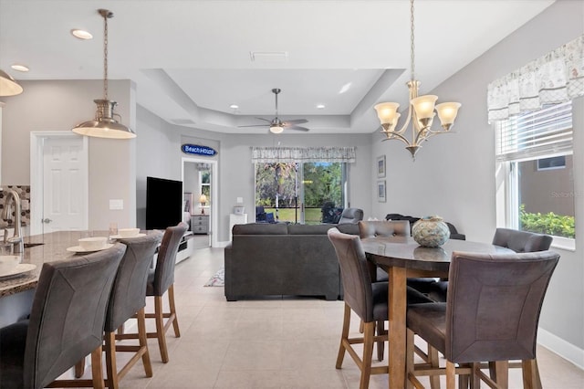 tiled dining area with ceiling fan with notable chandelier, a tray ceiling, and sink