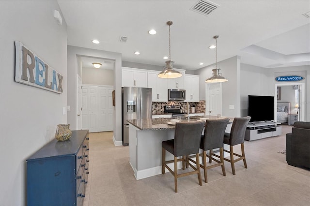 kitchen featuring appliances with stainless steel finishes, backsplash, pendant lighting, dark stone counters, and white cabinets