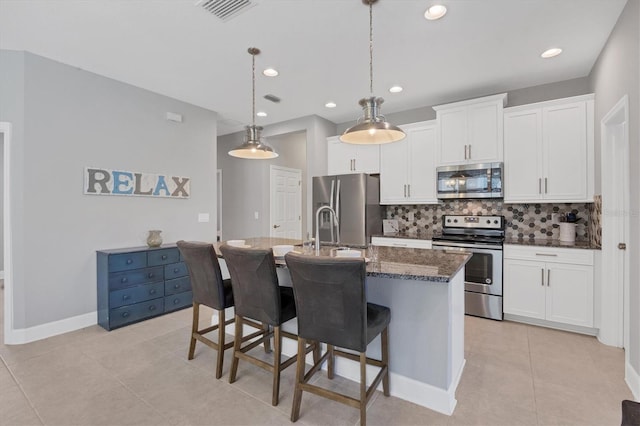 kitchen with appliances with stainless steel finishes, tasteful backsplash, an island with sink, white cabinets, and decorative light fixtures