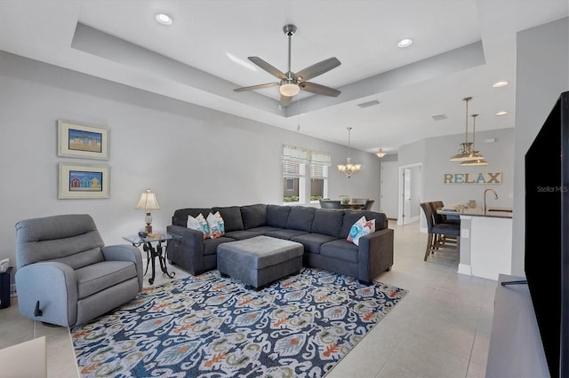 living room featuring a tray ceiling, light tile patterned floors, and ceiling fan with notable chandelier