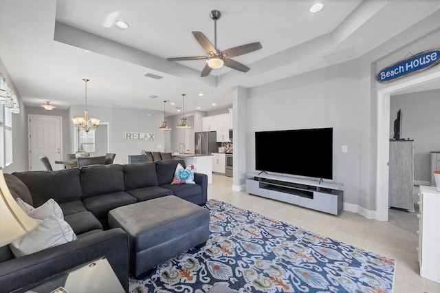 tiled living room featuring a tray ceiling, sink, and ceiling fan with notable chandelier