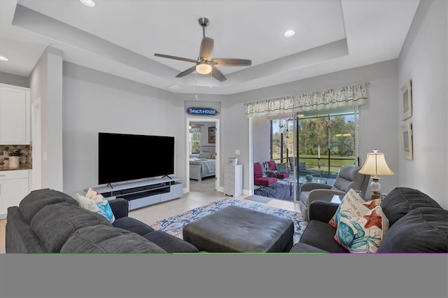 tiled living room with ceiling fan and a tray ceiling