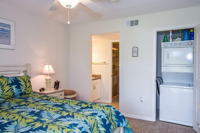 carpeted bedroom featuring a textured ceiling, ensuite bath, stacked washer / dryer, and ceiling fan