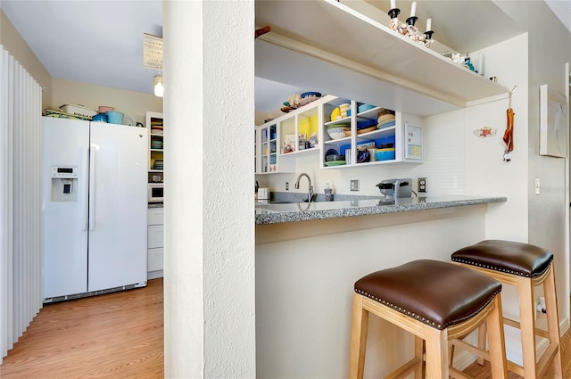 kitchen with a kitchen bar, light wood-type flooring, white refrigerator with ice dispenser, and light stone counters