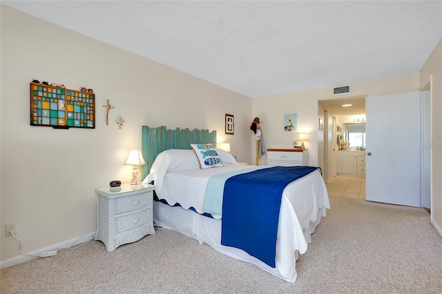 bedroom featuring ensuite bath, light colored carpet, and a textured ceiling