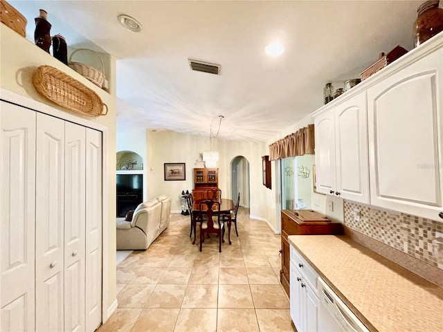 kitchen featuring stainless steel dishwasher, white cabinetry, hanging light fixtures, and light tile patterned floors