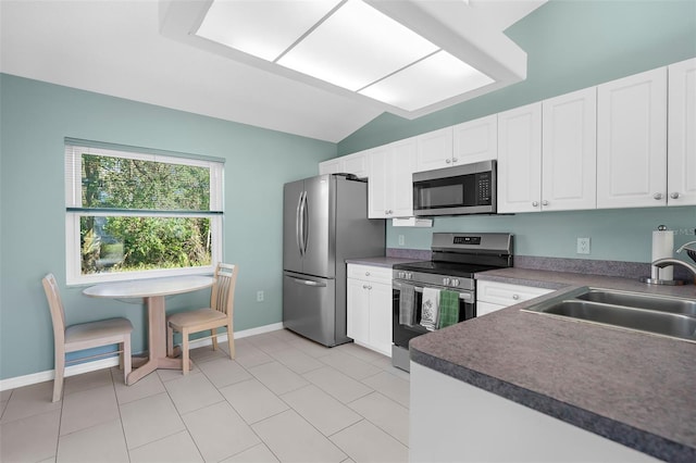 kitchen featuring sink, stainless steel appliances, light tile patterned floors, lofted ceiling, and white cabinets