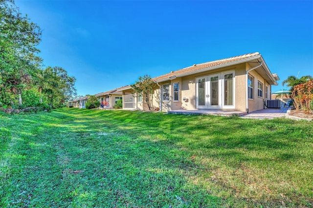 back of property with french doors, central air condition unit, and a lawn