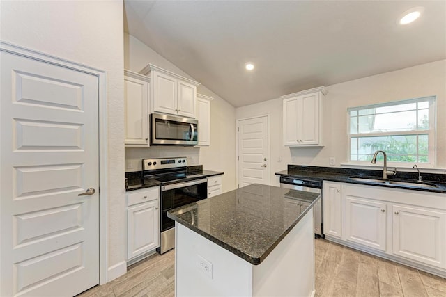 kitchen with lofted ceiling, white cabinets, sink, appliances with stainless steel finishes, and a kitchen island