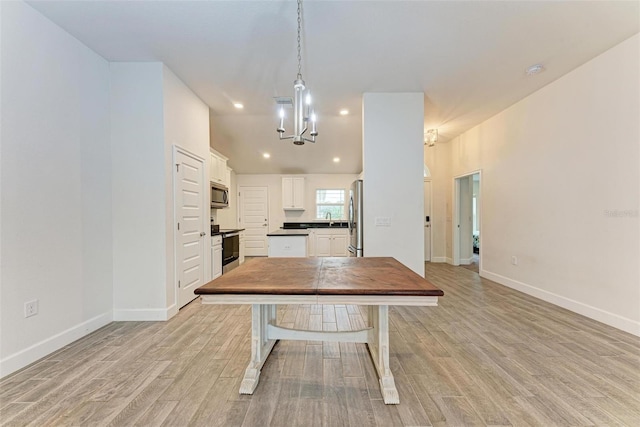 kitchen with light wood-type flooring, stainless steel appliances, sink, decorative light fixtures, and white cabinetry