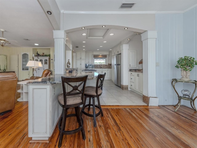 kitchen with stainless steel refrigerator, white cabinetry, light hardwood / wood-style flooring, and ornate columns