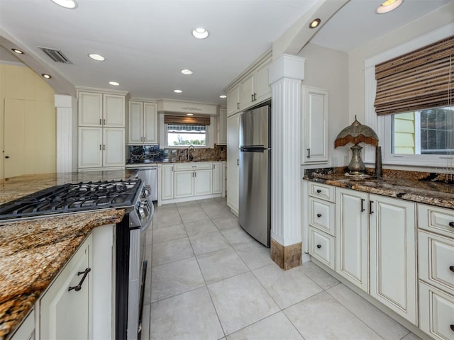 kitchen featuring decorative backsplash, light tile patterned floors, stainless steel appliances, and dark stone countertops