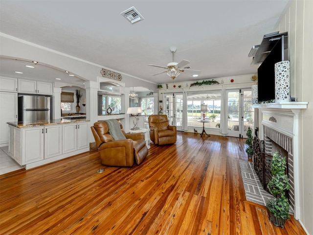 living room featuring ceiling fan, french doors, a brick fireplace, light hardwood / wood-style flooring, and ornamental molding