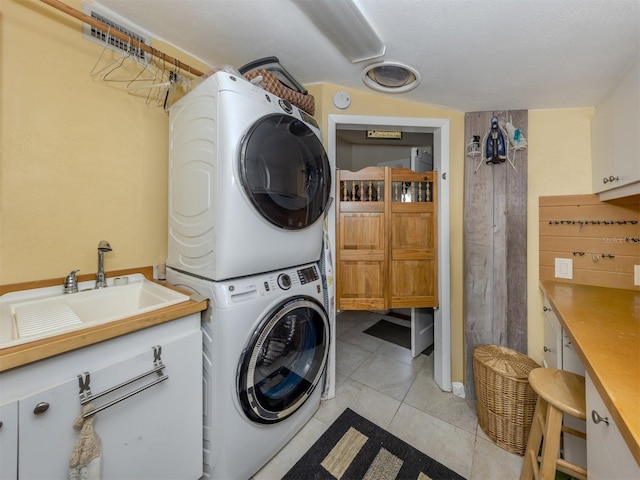 clothes washing area featuring sink, cabinets, a textured ceiling, stacked washer / drying machine, and light tile patterned floors