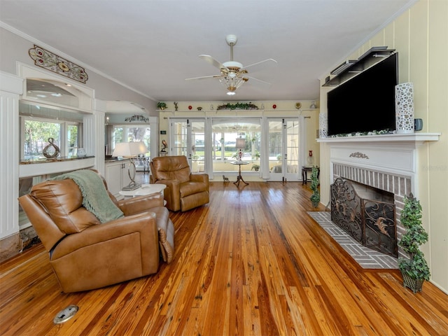 living room with ceiling fan, french doors, light hardwood / wood-style floors, a fireplace, and ornamental molding