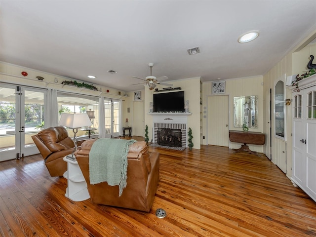 living room featuring a brick fireplace, ceiling fan, wood-type flooring, and french doors