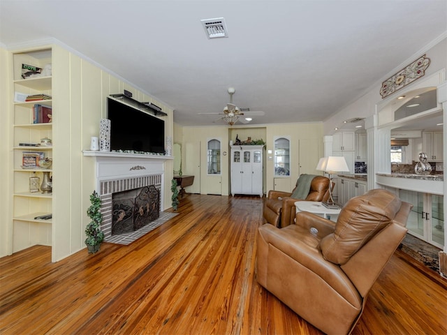 living room with a brick fireplace, ceiling fan, crown molding, and light hardwood / wood-style flooring