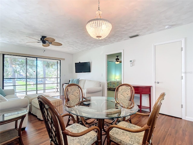 dining room with ceiling fan with notable chandelier, a textured ceiling, and dark hardwood / wood-style floors