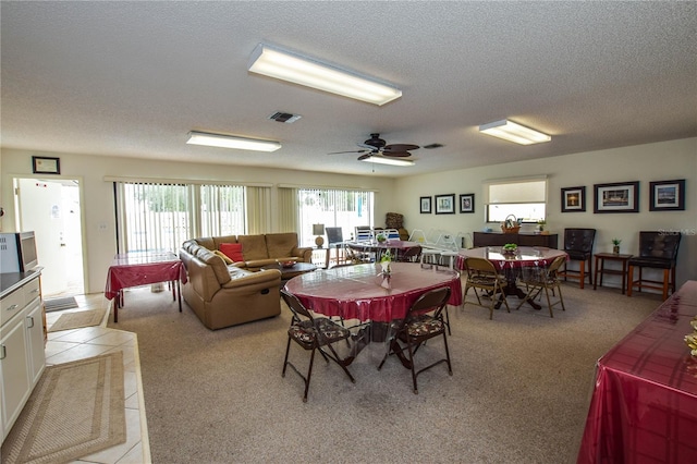 dining space with ceiling fan, light colored carpet, and a textured ceiling