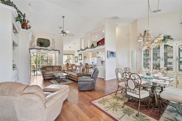 living room featuring ceiling fan with notable chandelier, wood-type flooring, and a high ceiling