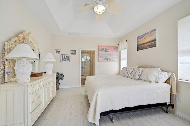 bedroom featuring light wood-type flooring, a tray ceiling, and ceiling fan