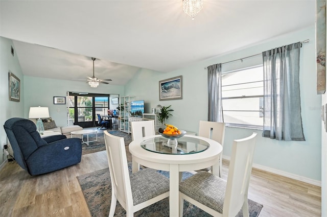 dining space with ceiling fan with notable chandelier, light hardwood / wood-style floors, and lofted ceiling