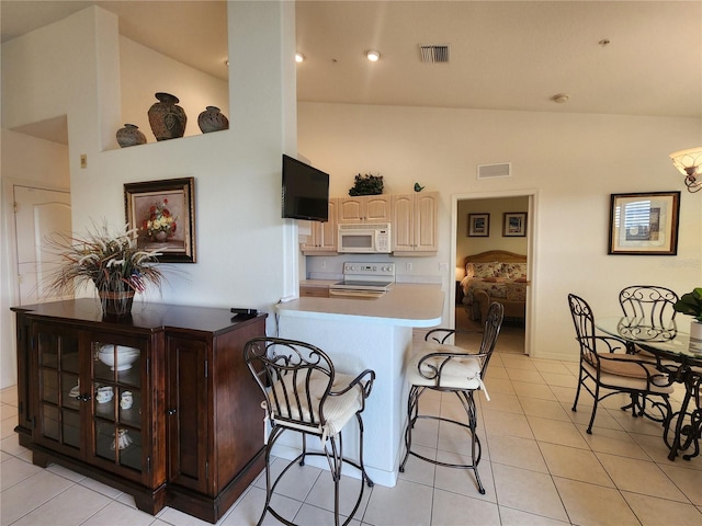 kitchen with a breakfast bar area, high vaulted ceiling, light tile patterned floors, kitchen peninsula, and white appliances