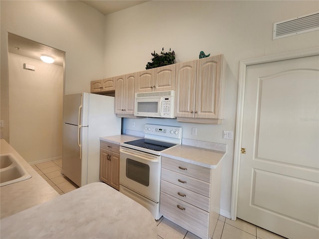 kitchen with light tile patterned flooring, sink, light brown cabinets, and white appliances