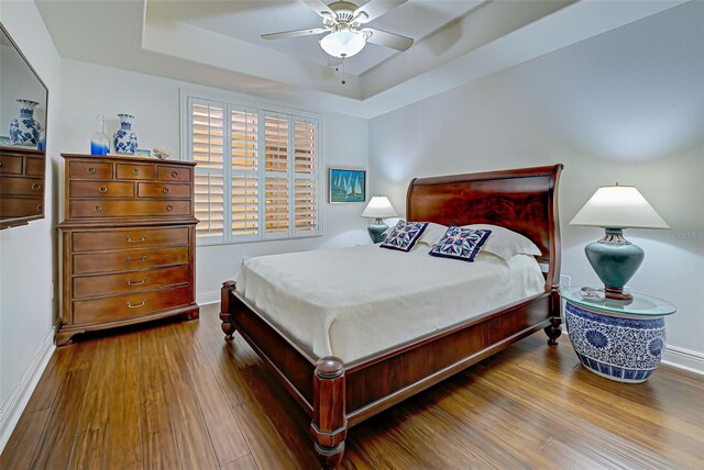 bedroom with hardwood / wood-style flooring, ceiling fan, and a tray ceiling