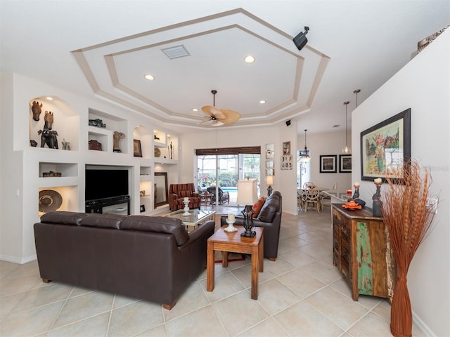 tiled living room featuring ceiling fan, a raised ceiling, and built in shelves