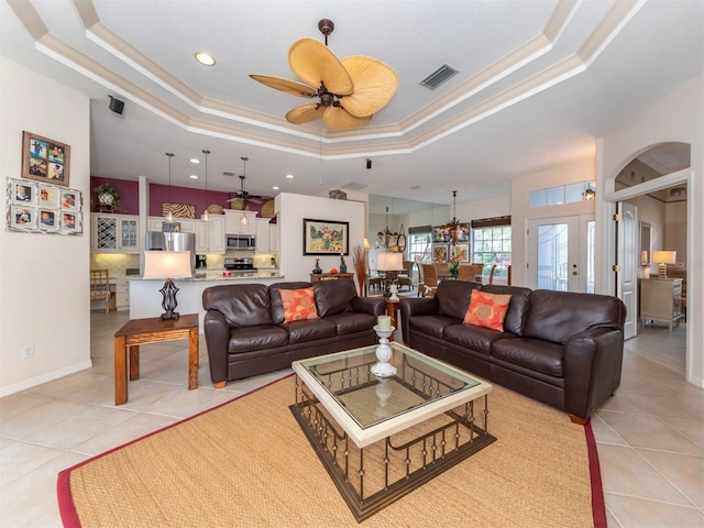 living room with a raised ceiling, ceiling fan, and light tile patterned flooring