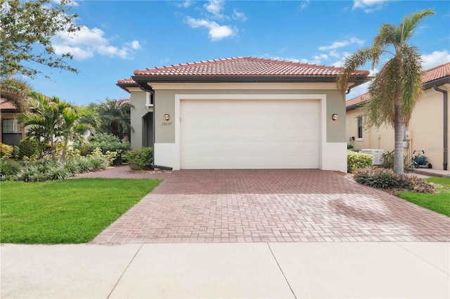 mediterranean / spanish home with decorative driveway, a tile roof, stucco siding, an attached garage, and a front lawn