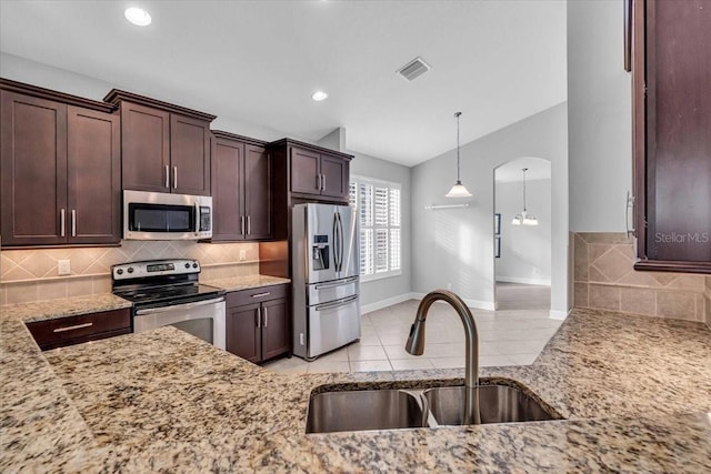 kitchen featuring sink, hanging light fixtures, light stone counters, light tile patterned floors, and appliances with stainless steel finishes