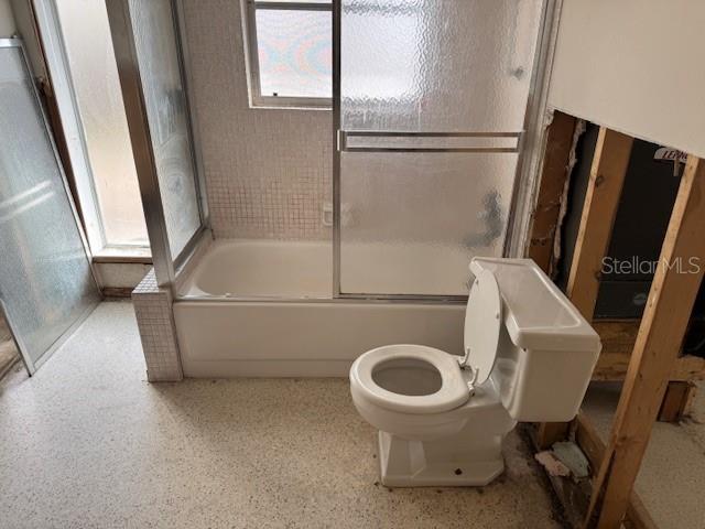 bathroom with toilet and bath / shower combo with glass door