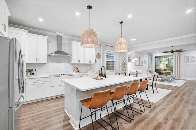 kitchen with stainless steel fridge, wall chimney range hood, pendant lighting, light hardwood / wood-style floors, and white cabinetry