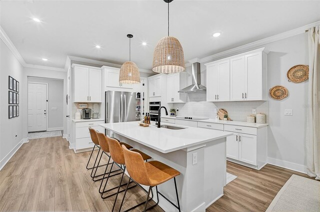 kitchen featuring white cabinets, decorative light fixtures, stainless steel refrigerator, and wall chimney range hood