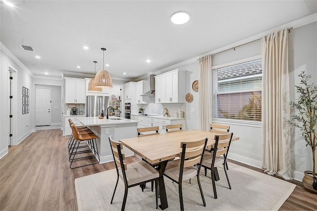 dining area featuring light wood-type flooring, ornamental molding, and sink