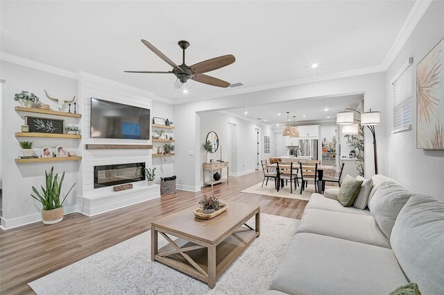 living room with a fireplace, hardwood / wood-style flooring, ceiling fan, and ornamental molding