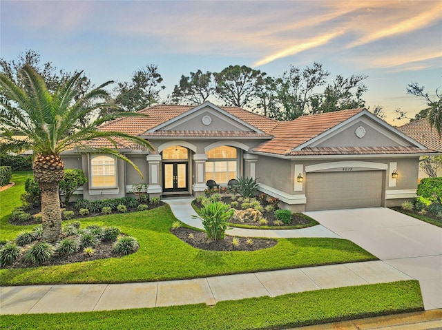 mediterranean / spanish house with a garage, a yard, and french doors