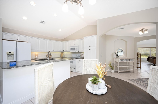 kitchen featuring dark stone counters, white appliances, sink, white cabinets, and lofted ceiling