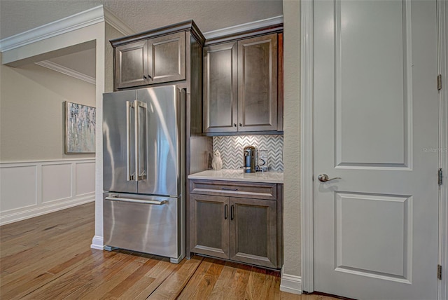 kitchen featuring crown molding, high end refrigerator, dark brown cabinets, light hardwood / wood-style floors, and backsplash