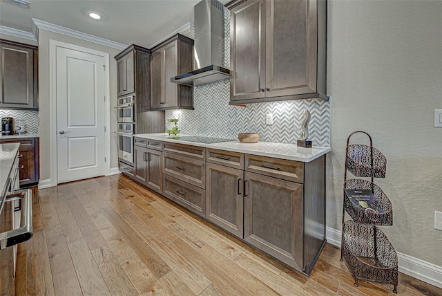 kitchen featuring dark brown cabinets, light hardwood / wood-style flooring, black electric stovetop, decorative backsplash, and wall chimney range hood