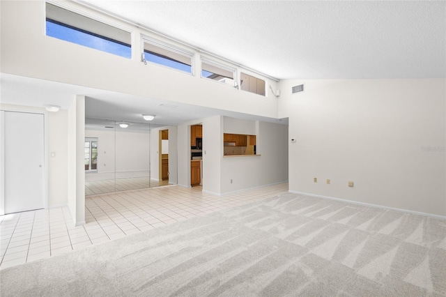 unfurnished living room with light colored carpet, a textured ceiling, and high vaulted ceiling