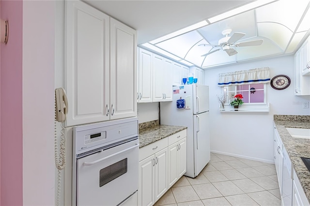 kitchen with light stone counters, white appliances, ceiling fan, white cabinets, and light tile patterned flooring