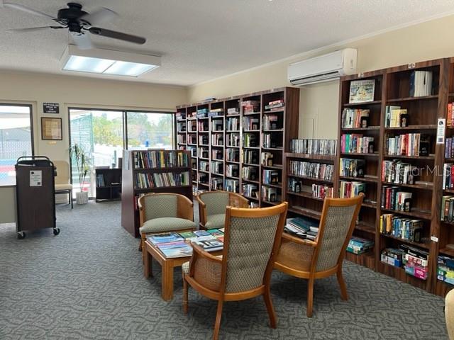 612 Bird Bay Dr S Unit 114, Venice, FL 34285 - sitting room featuring an AC wall unit, wall of books, carpet floors, and a ceiling fan
