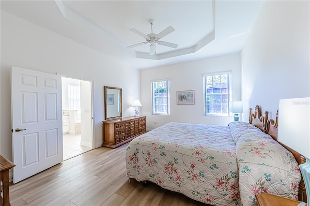 bedroom featuring connected bathroom, light hardwood / wood-style floors, a raised ceiling, and ceiling fan