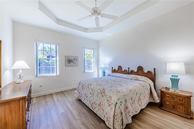 bedroom featuring light wood-type flooring, a tray ceiling, and ceiling fan