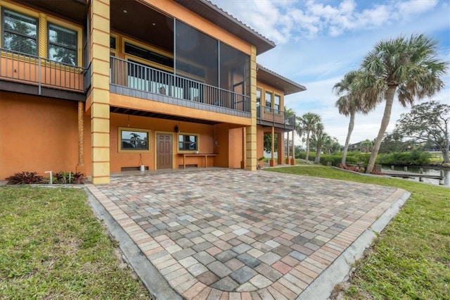 rear view of property featuring a lawn, a sunroom, a water view, and a patio