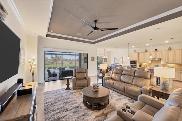 tiled living room featuring ceiling fan, ornamental molding, and a tray ceiling