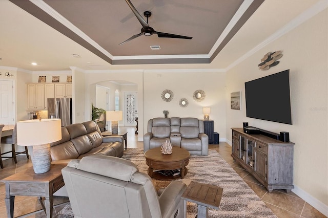 living room with light tile patterned floors, a tray ceiling, ceiling fan, and ornamental molding